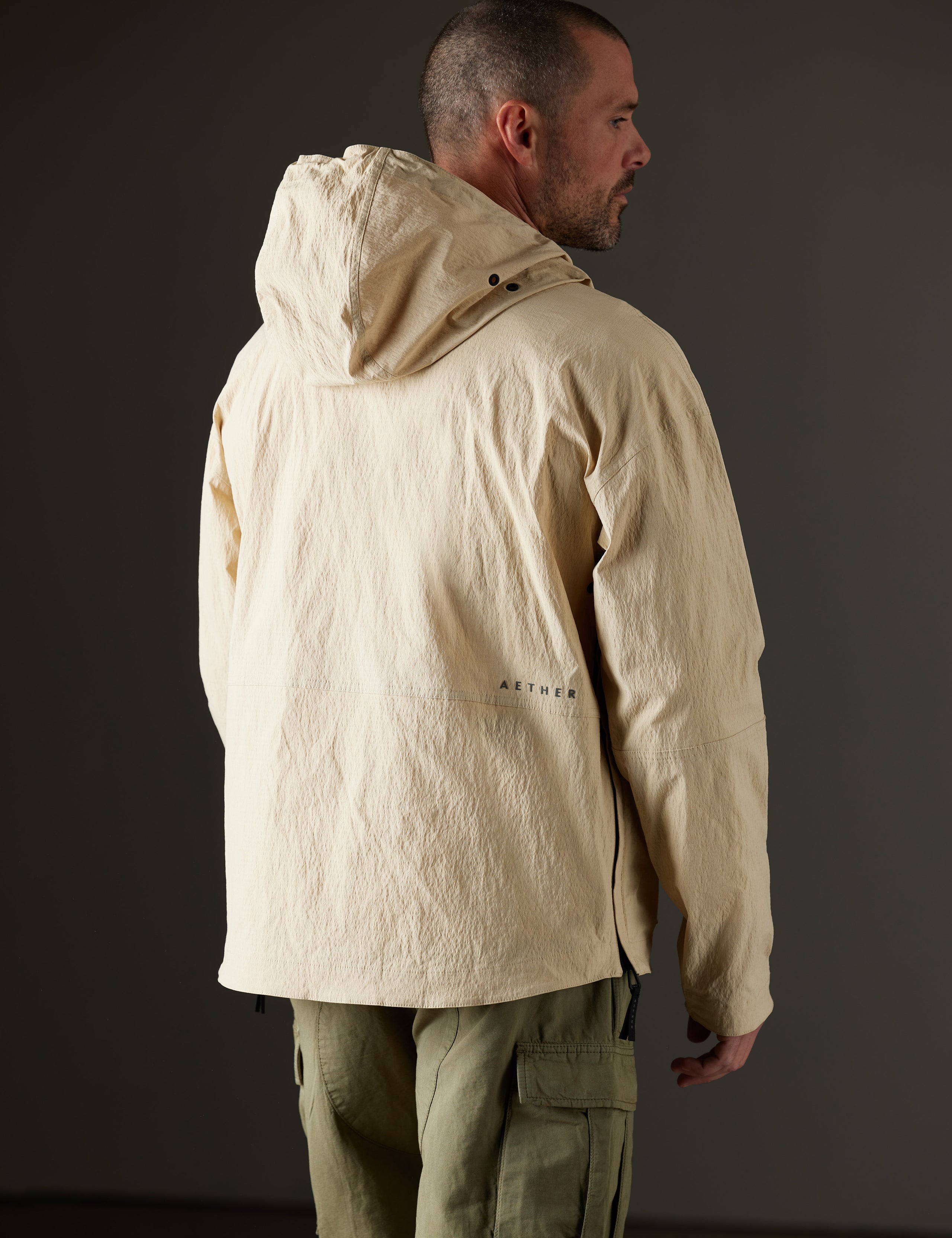 Rear 3/4 body view of man wearing Harrier Anorak in Desert Tan from AETHER Apparel.