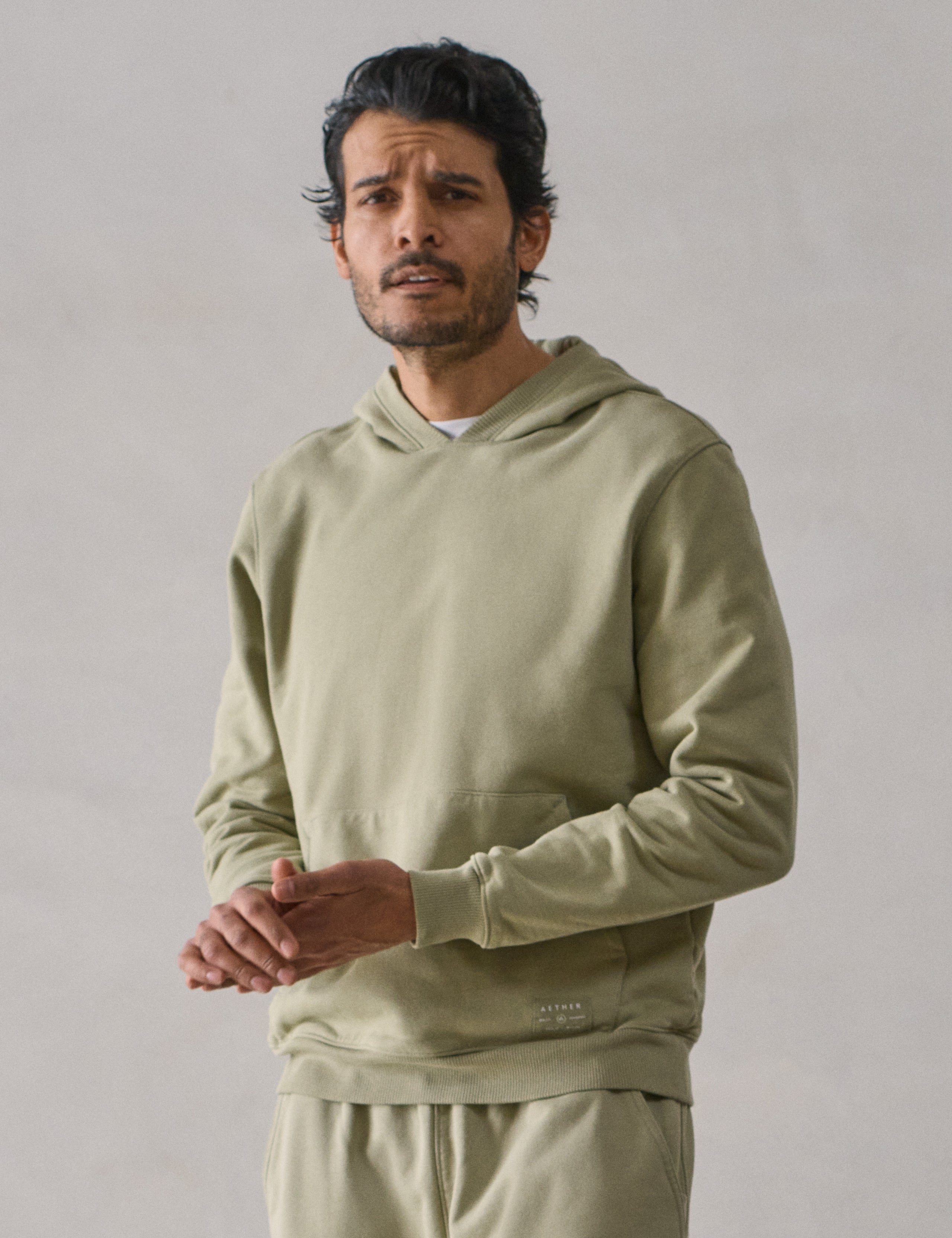 Front upper body view of man wearing Osa Pullover Hoodie in Sage Green from AETHER Apparel.