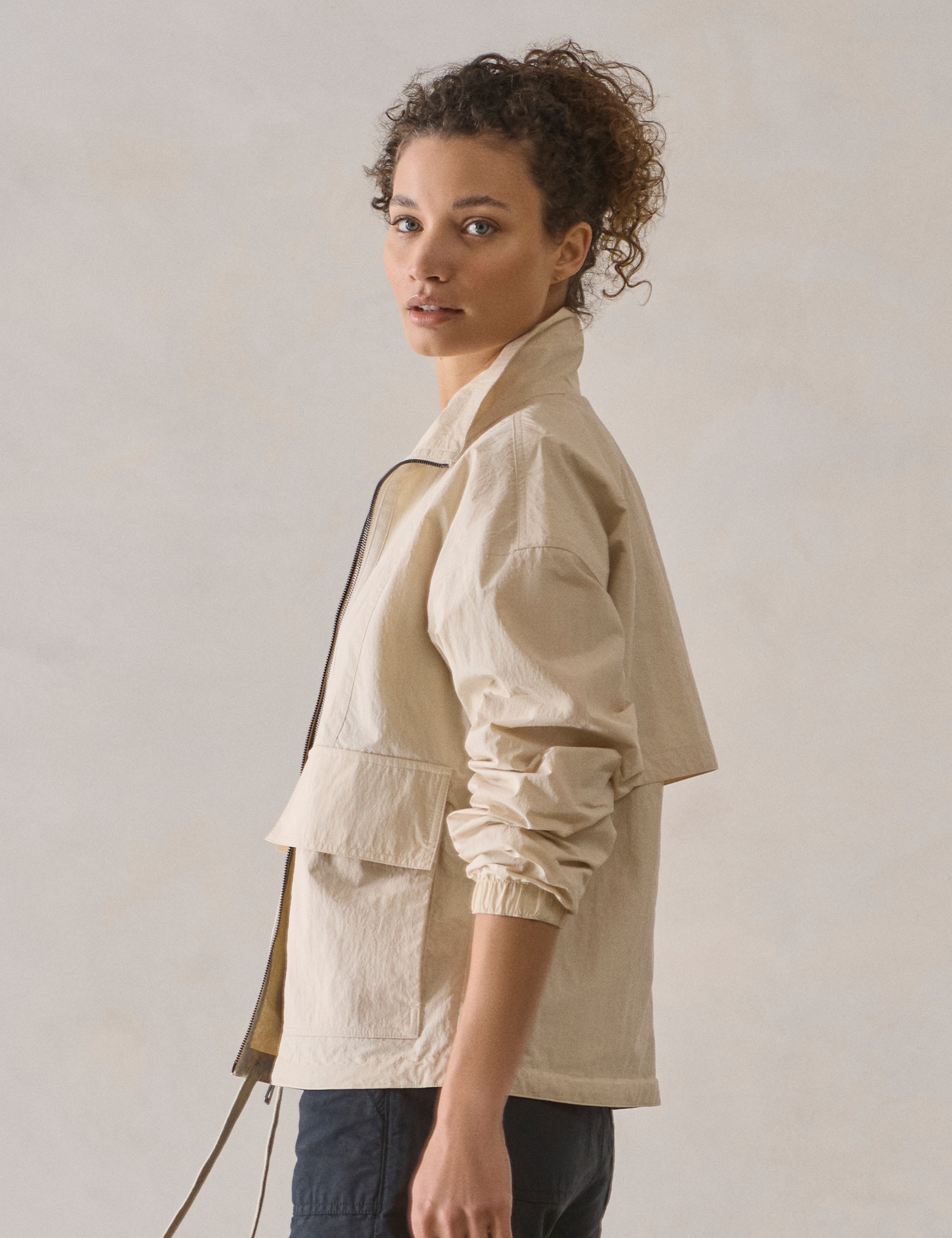 Left side profile view of woman wearing Mila Windbreaker in Bone white from AETHER Apparel.