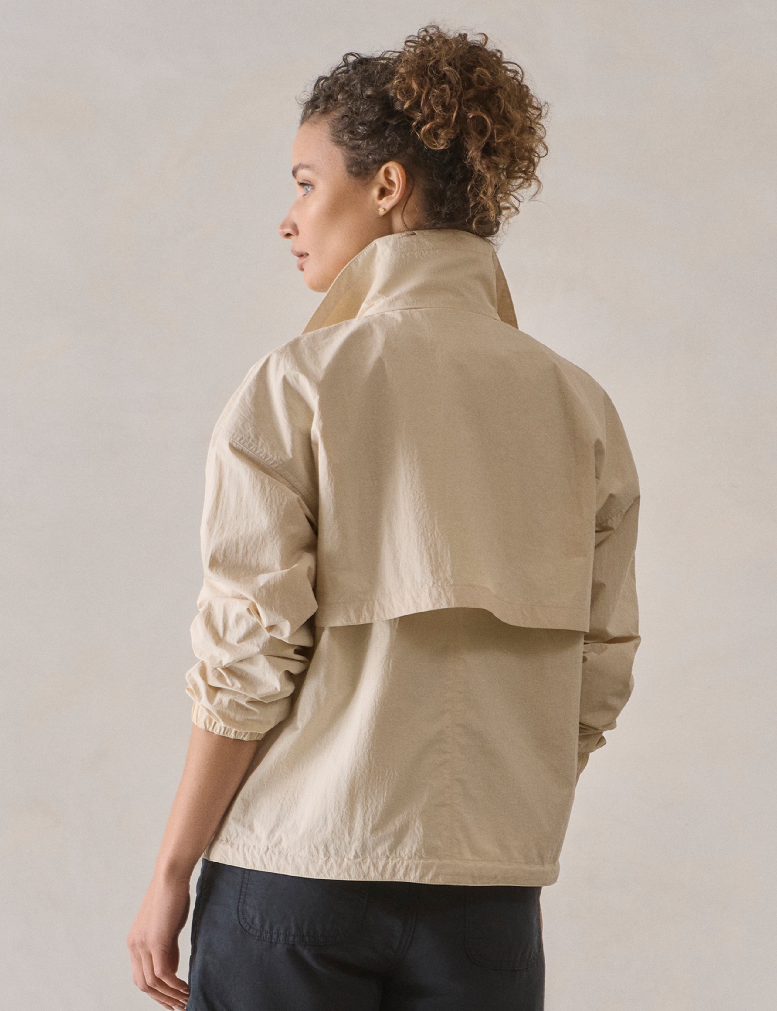 Rear 3/4 view of woman wearing Mila Windbreaker in Bone white from AETHER Apparel.