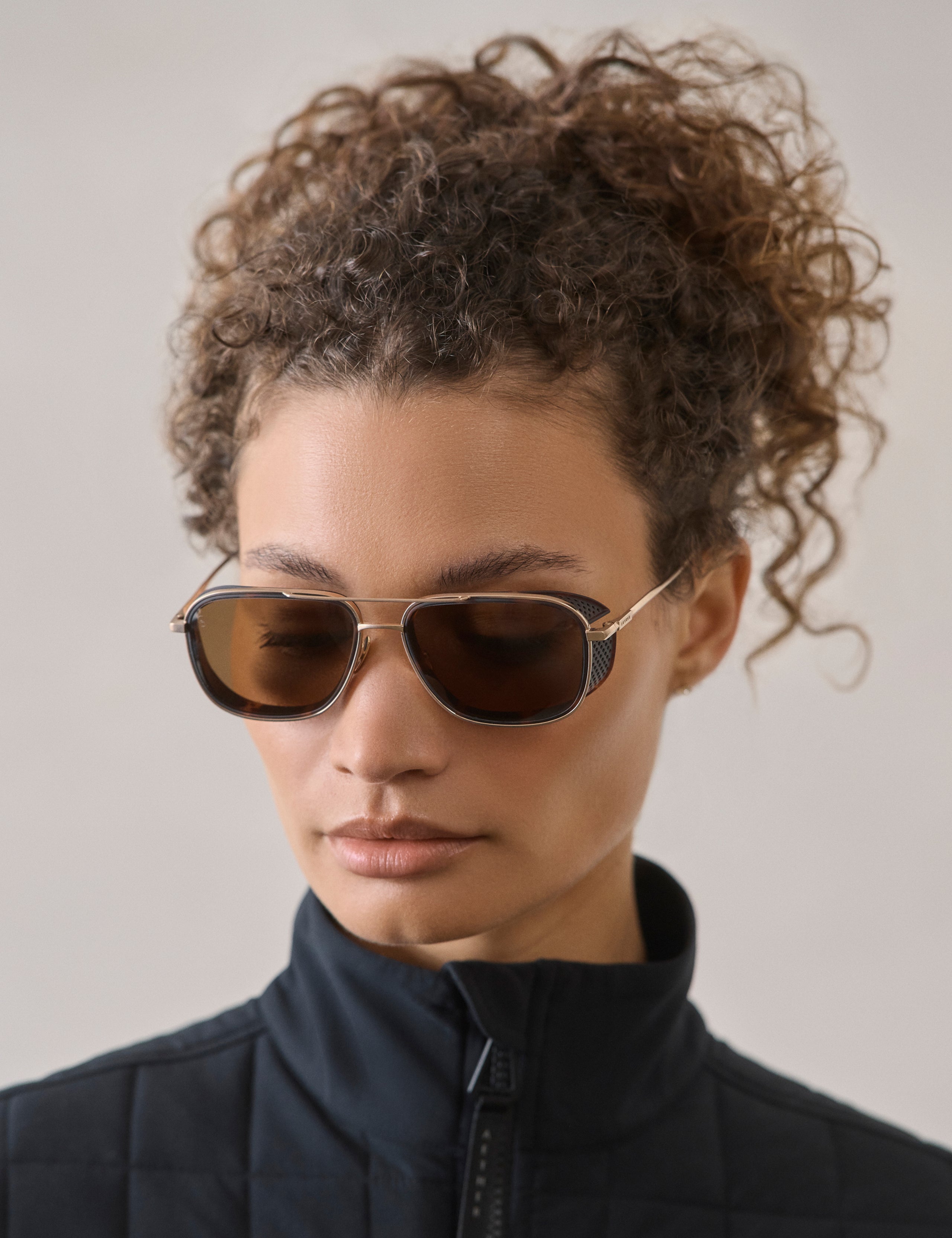Front 3/4 view of woman wearing Summit Sunglass in Brushed Gold titanium with G15 Lens from AETHER Apparel.