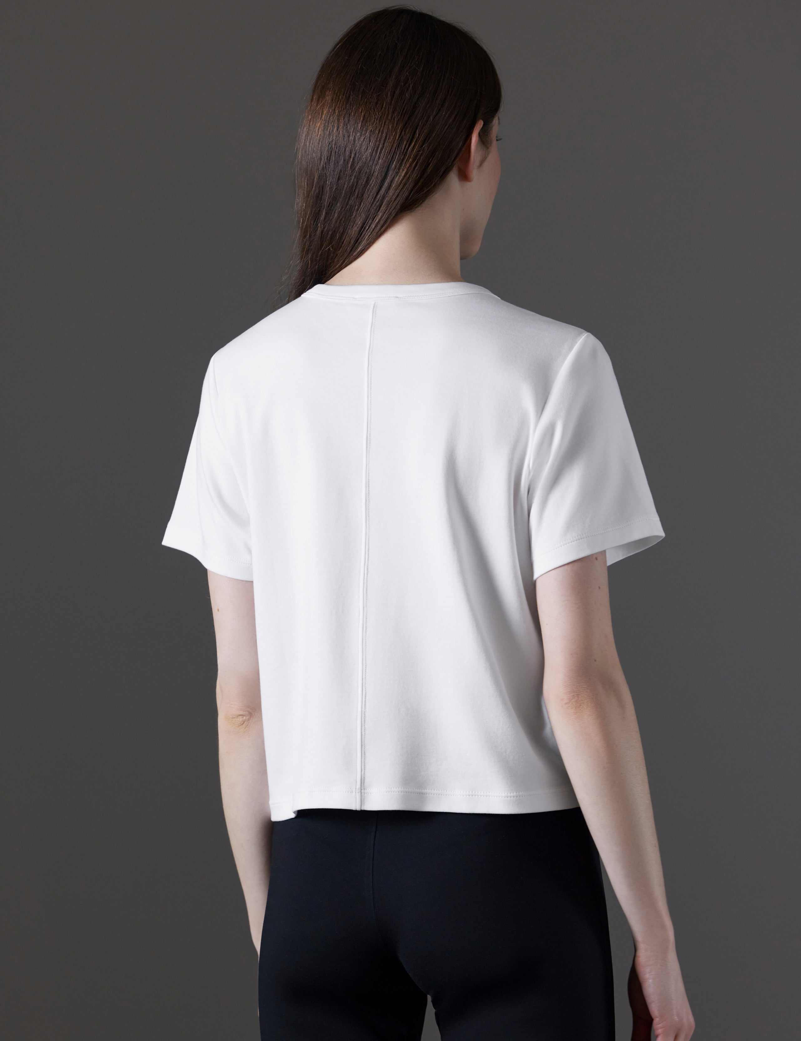 Rear angled view of woman wearing Emery Pima Cropped Tee in White from AETHER Apparel.