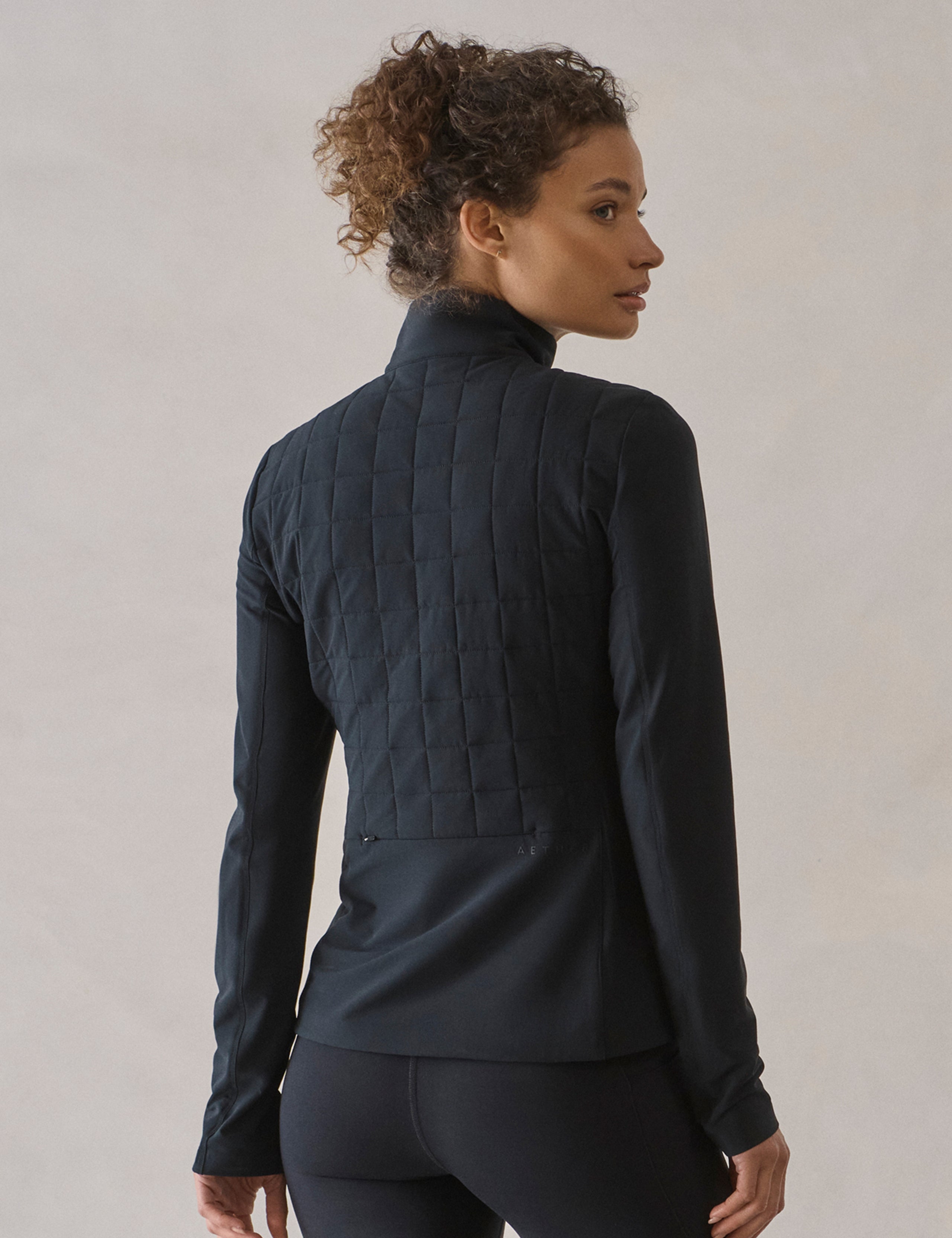 Rear 3/4 body view of woman wearing Wren Insulated Half-Zip in Onyx Black from AETHER Apparel.